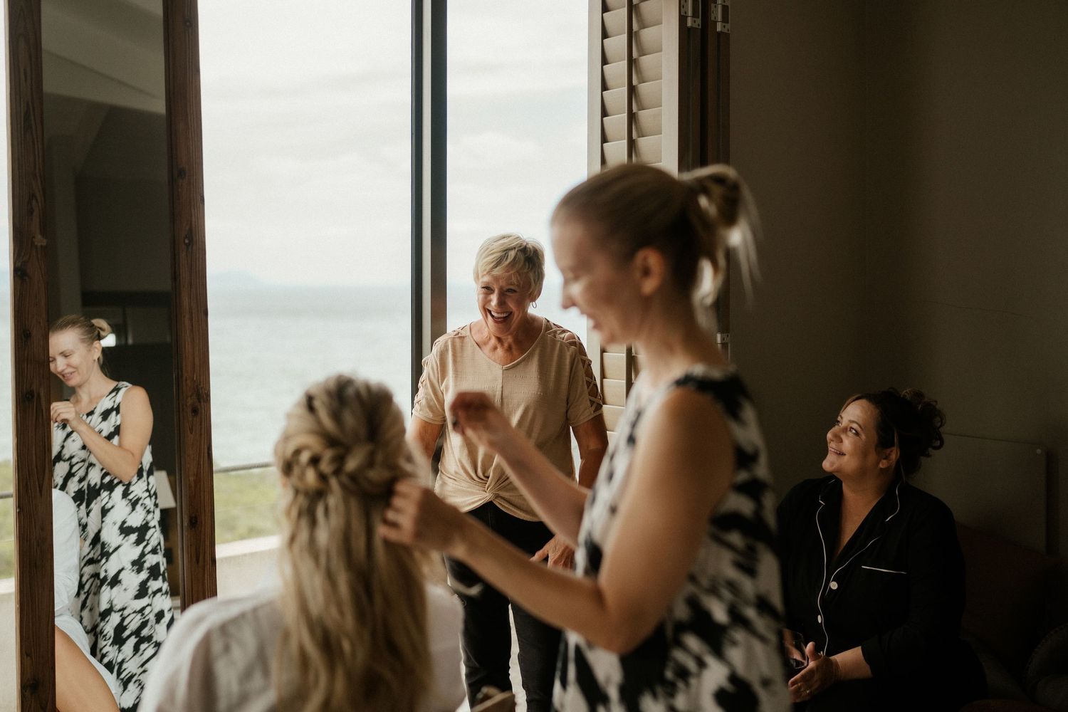 A group of people gather in a bright room with ocean views getting ready for a special occasion.