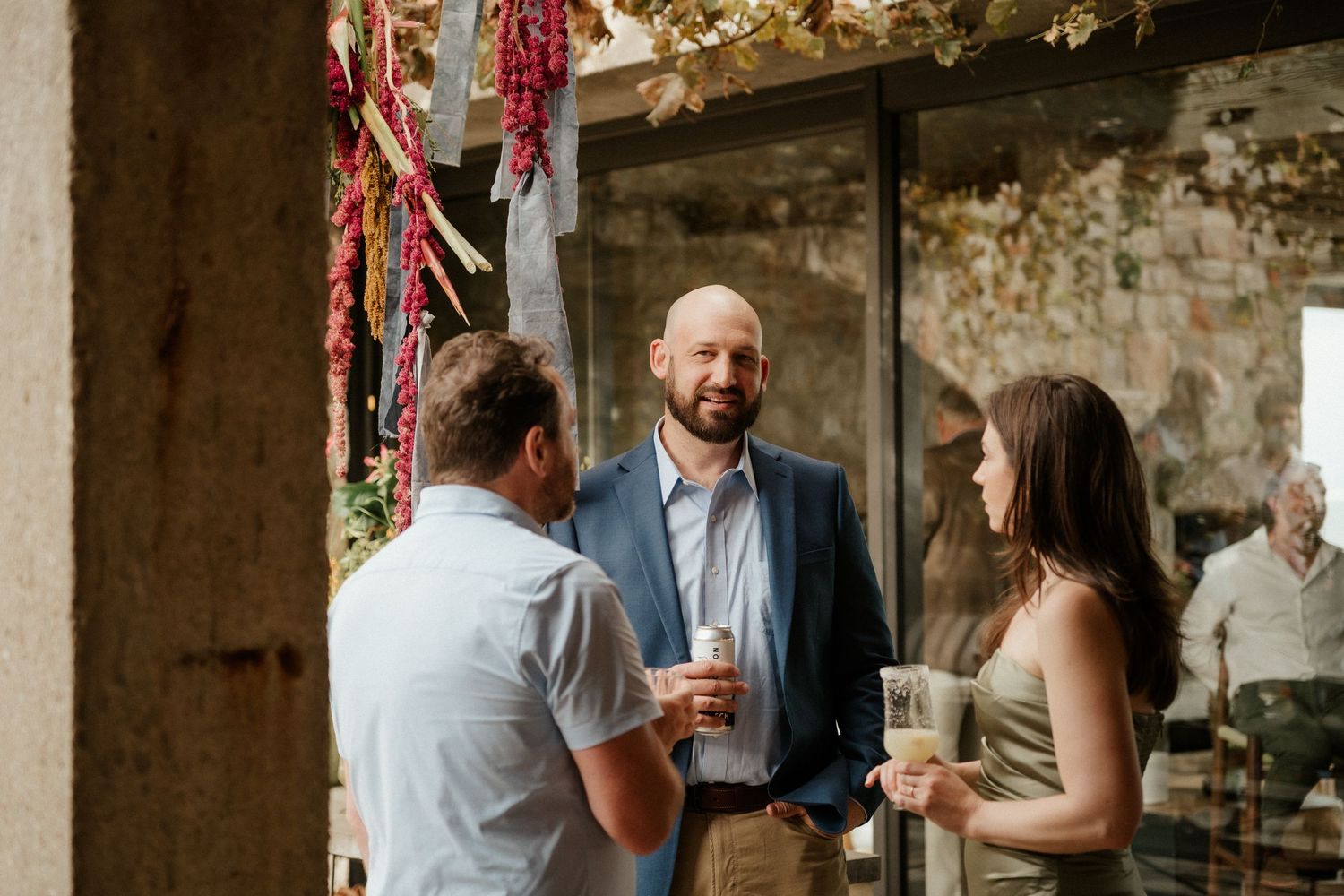 Guests enjoying casual conversation at a rustic wedding reception with string lights and exposed stone walls.