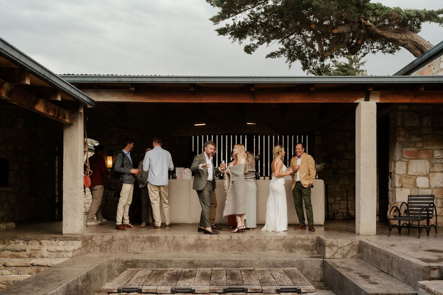 Wedding guests gathered at covered outdoor stone patio during reception.