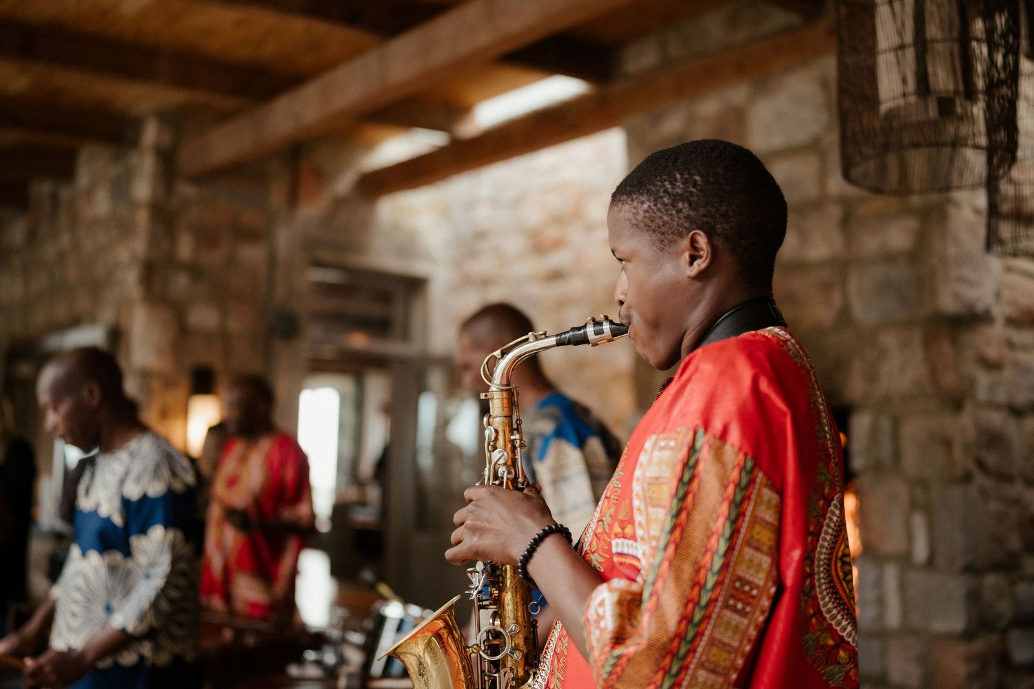 Young musician playing saxophone in vibrant orange attire at stone venue.
