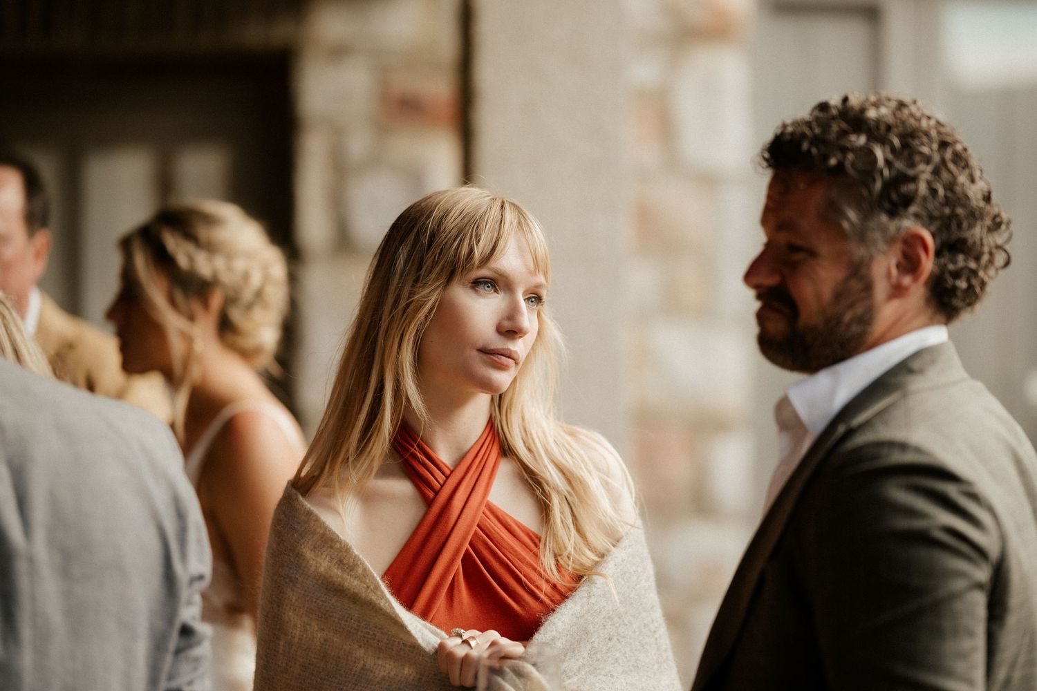 Wedding guests in formal attire having conversation at rustic stone venue.