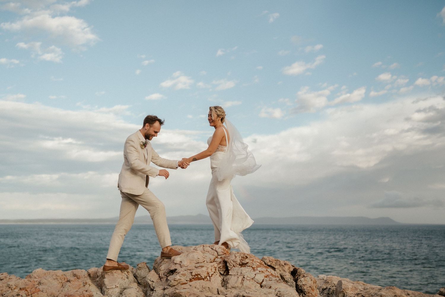 A romantic couple dances together on coastal rocks overlooking the ocean during their wedding celebration.