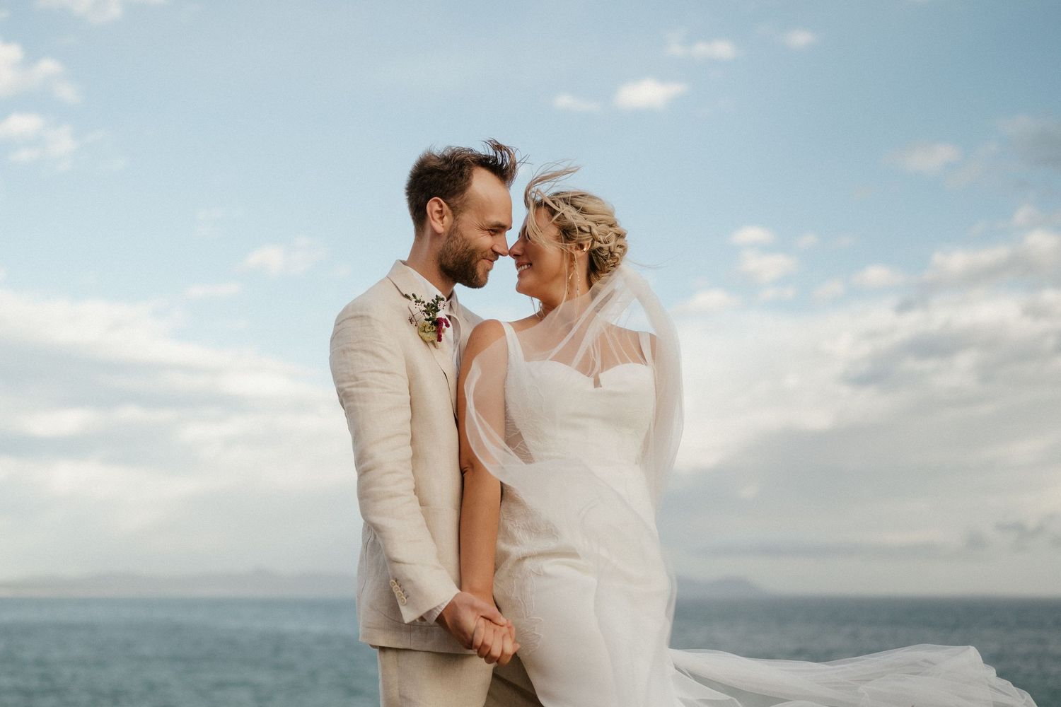 Romantic coastal wedding portrait with ocean and blue sky backdrop.