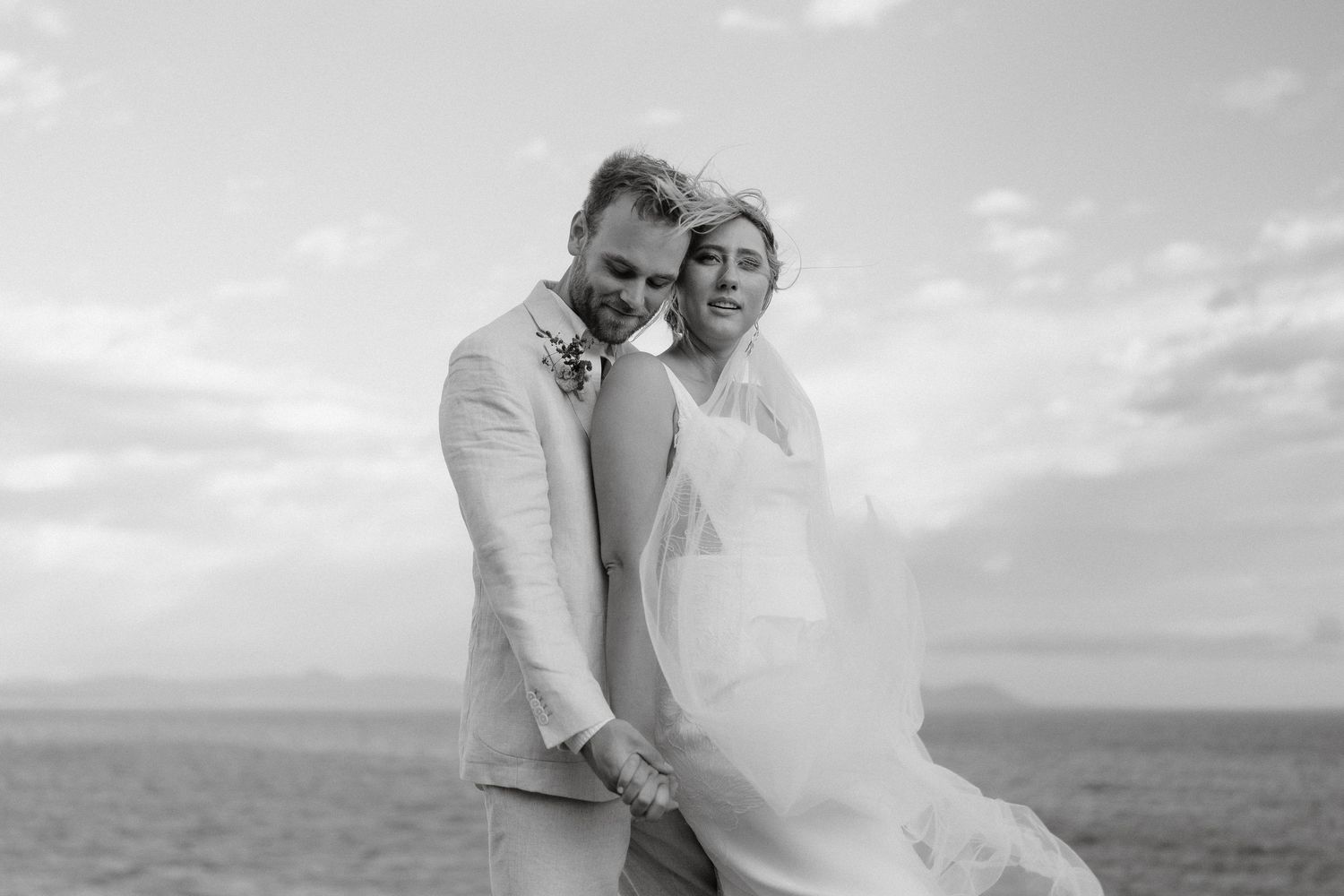 A black and white wedding portrait captured against a scenic coastal backdrop.