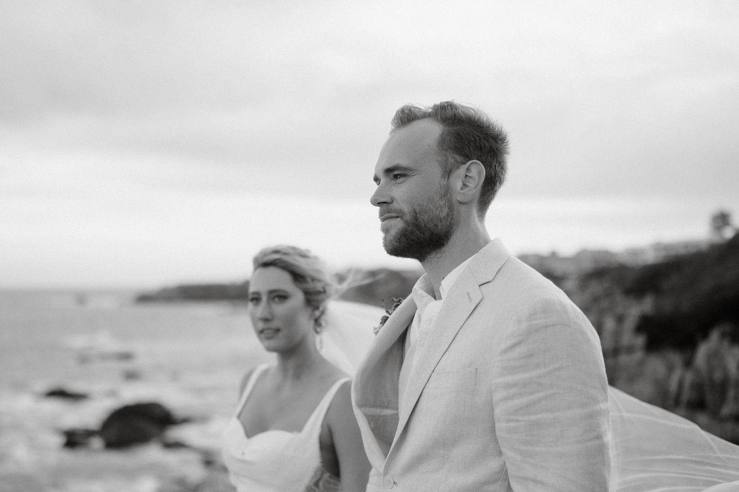 Black and white portrait of newlyweds looking out over coastal cliffs.