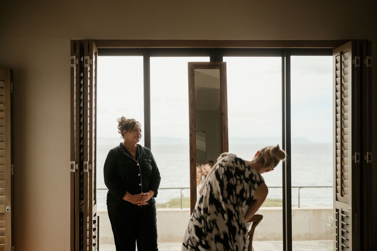 Two people stand silhouetted against large glass doors overlooking a scenic ocean view.
