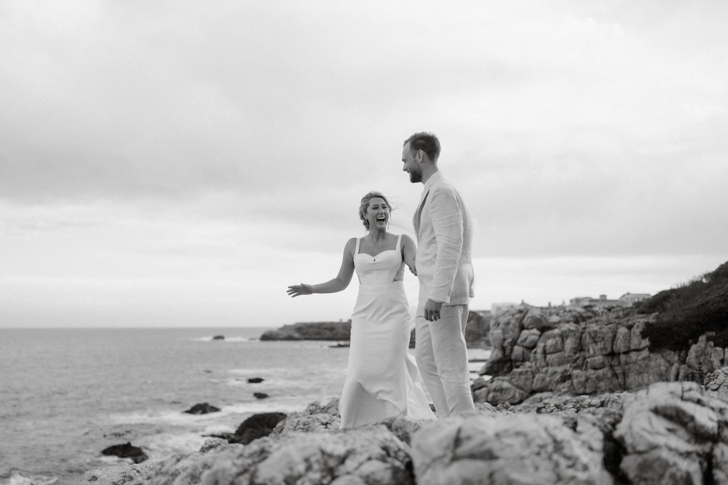 A coastal wedding portrait with the couple standing on rocky cliffs overlooking the ocean.
