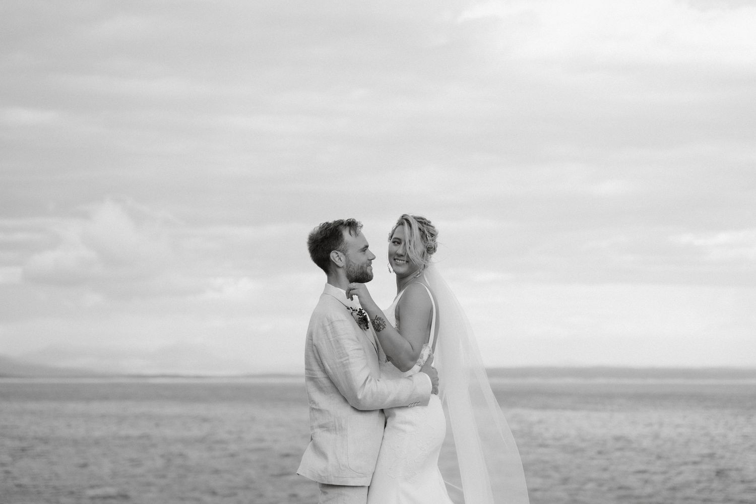 Black and white portrait of bride and groom embracing against dramatic sky.