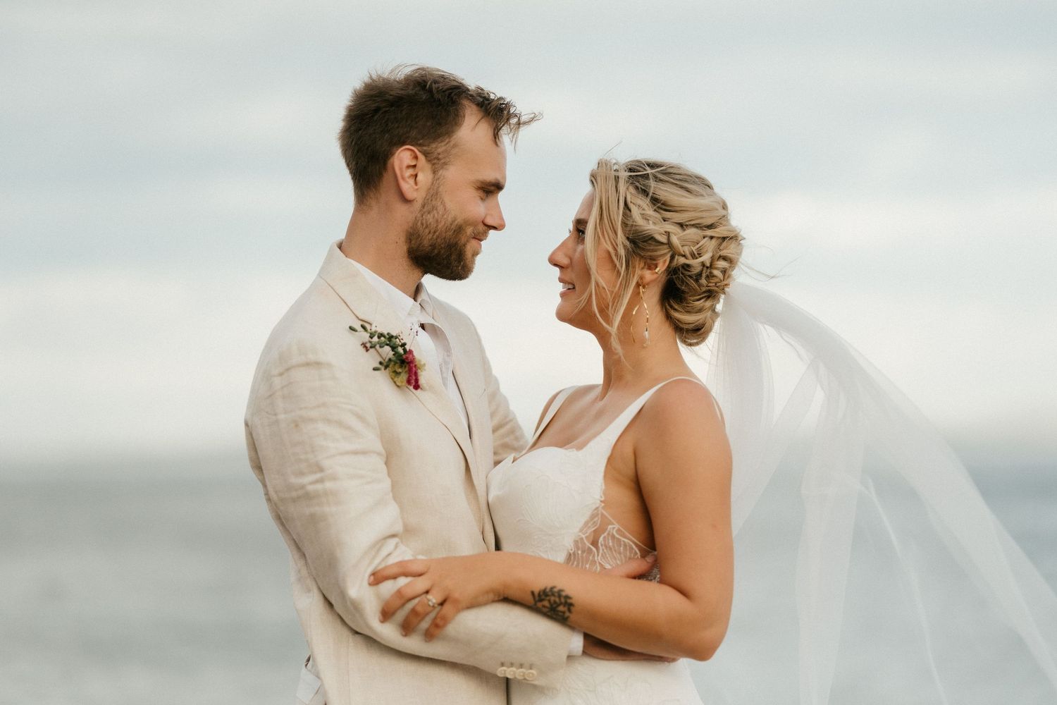 A romantic seaside wedding moment with a couple embracing against a cloudy sky.