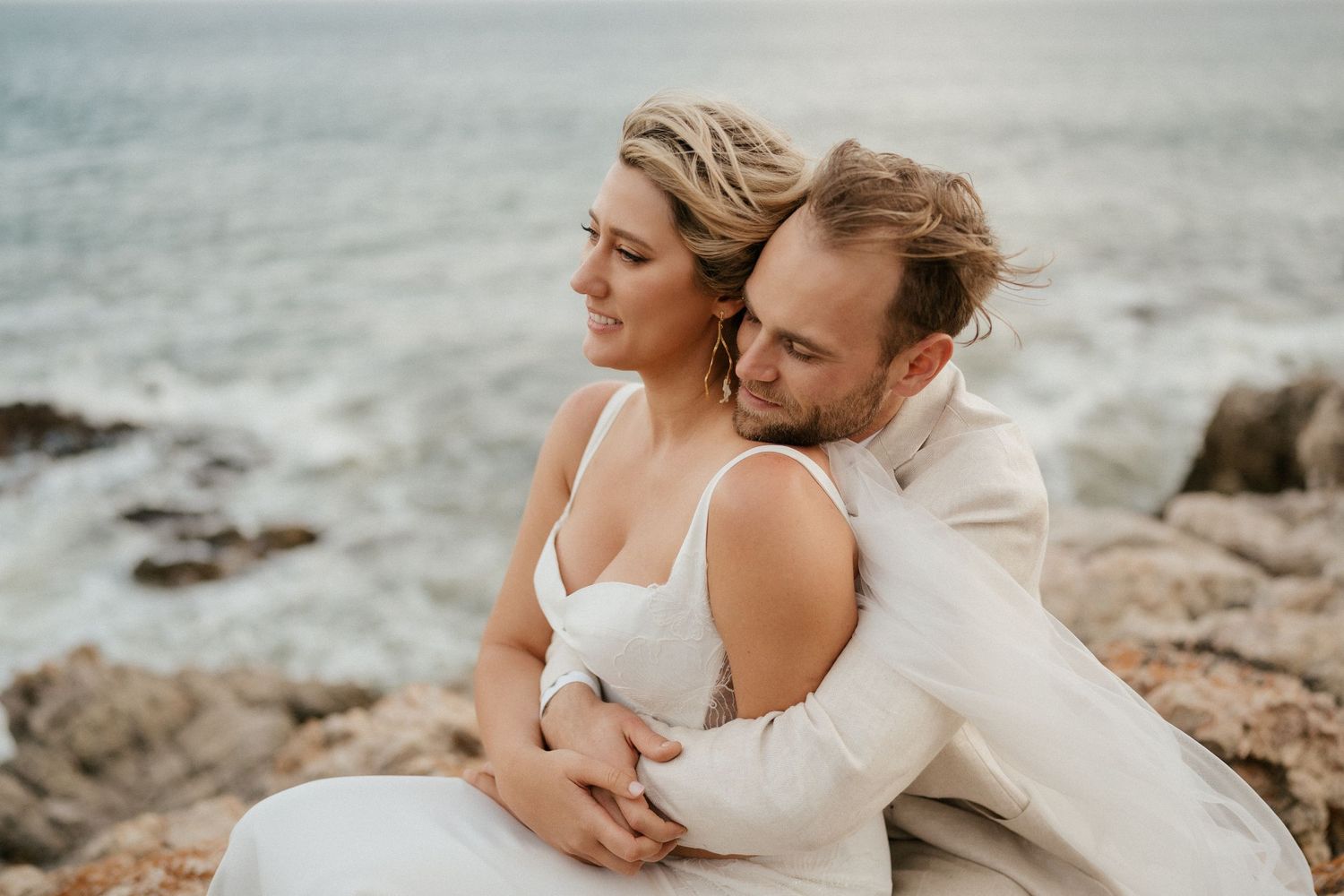 A couple shares an intimate moment on rocky coastal cliffs during their wedding.