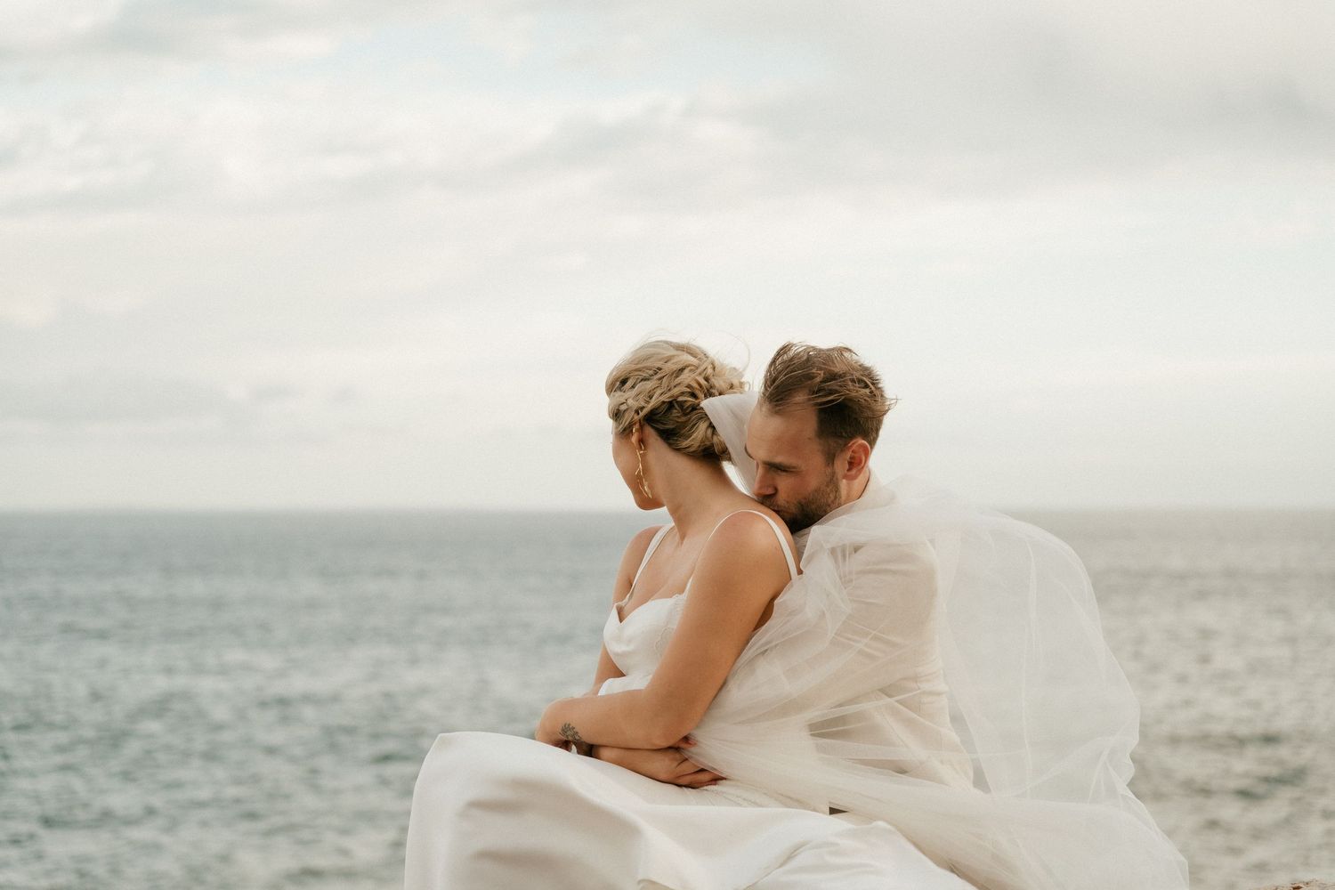 Newlyweds share an intimate moment by the ocean on their wedding day.