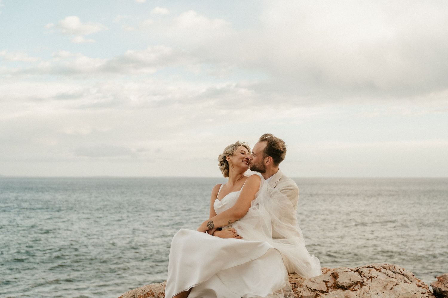 A romantic moment shared between newlyweds on coastal rocks at sunset.
