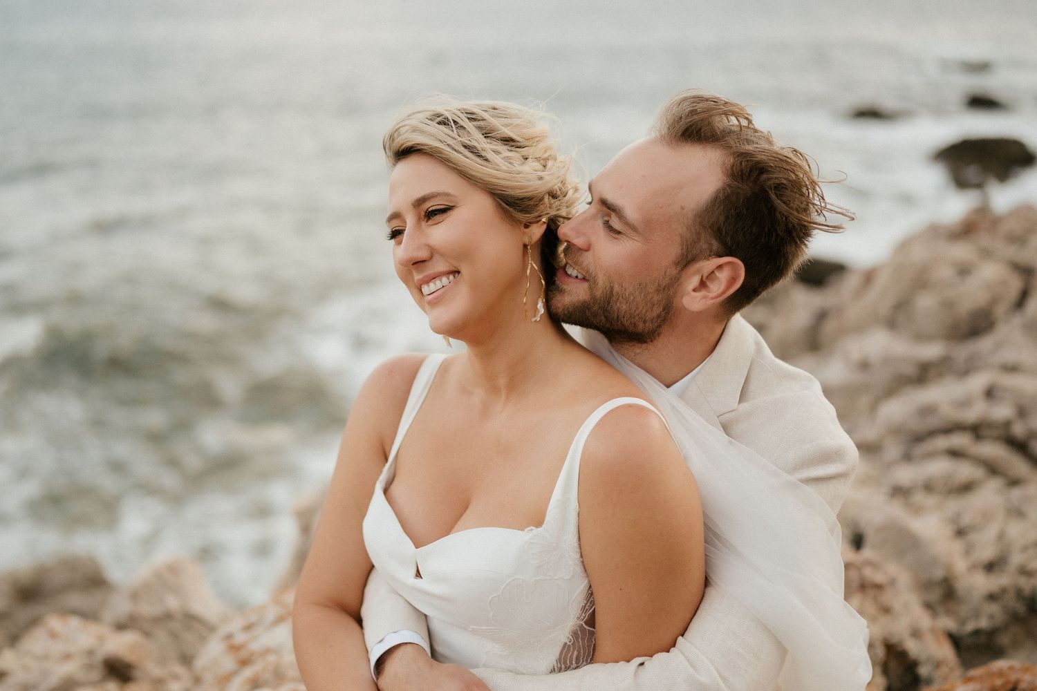 A romantic moment captured between a couple on rocky coastal cliffs during sunset.