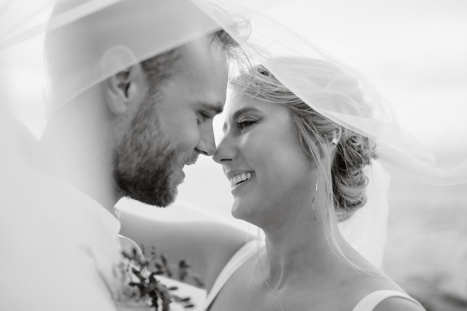 Black and white portrait of a tender moment between newlyweds under a veil.