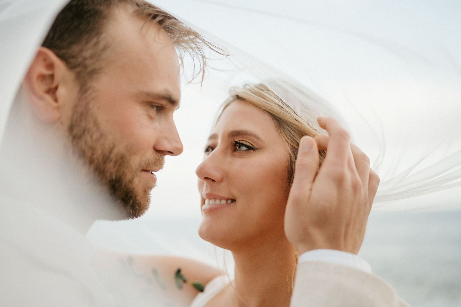 Intimate wedding portrait with bride's veil flowing in the ocean breeze.