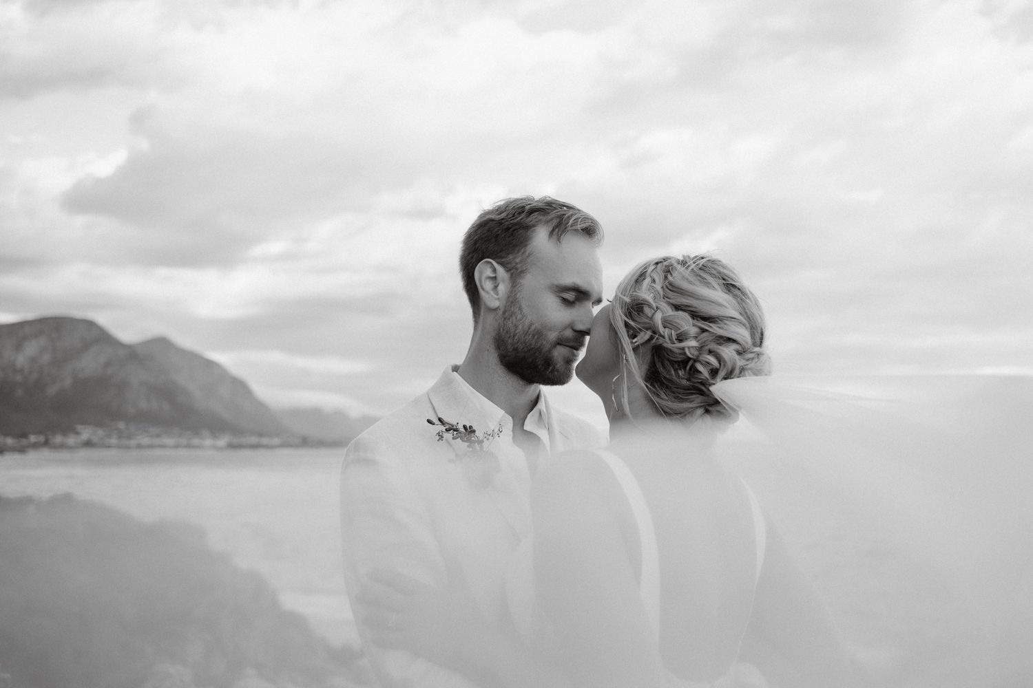 Black and white intimate portrait of couple against misty coastal mountain backdrop.