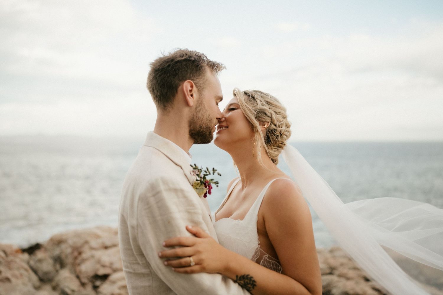 Romantic seaside moment captured between couple in light-colored wedding attire.