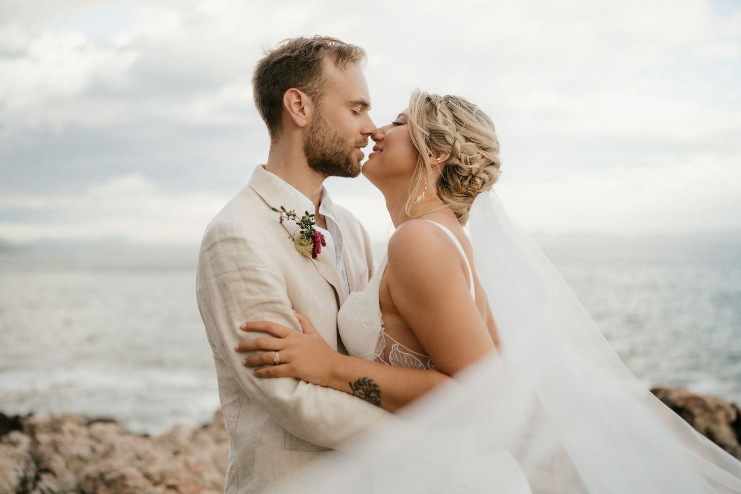 A romantic seaside wedding portrait with the couple embracing against an ocean backdrop.