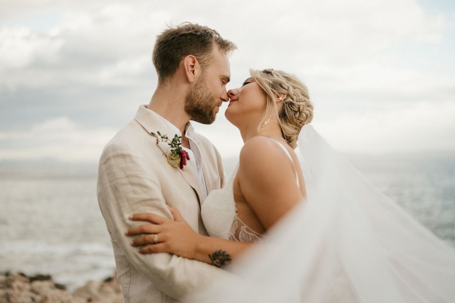 Romantic seaside wedding portrait with flowing veil and natural coastal backdrop.