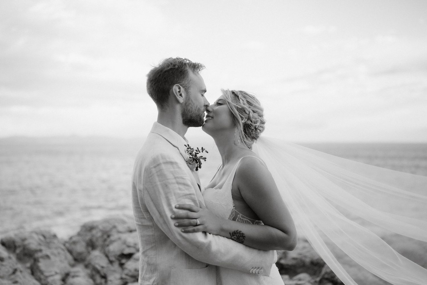 A romantic black and white portrait of a couple embracing on a windswept hilltop.