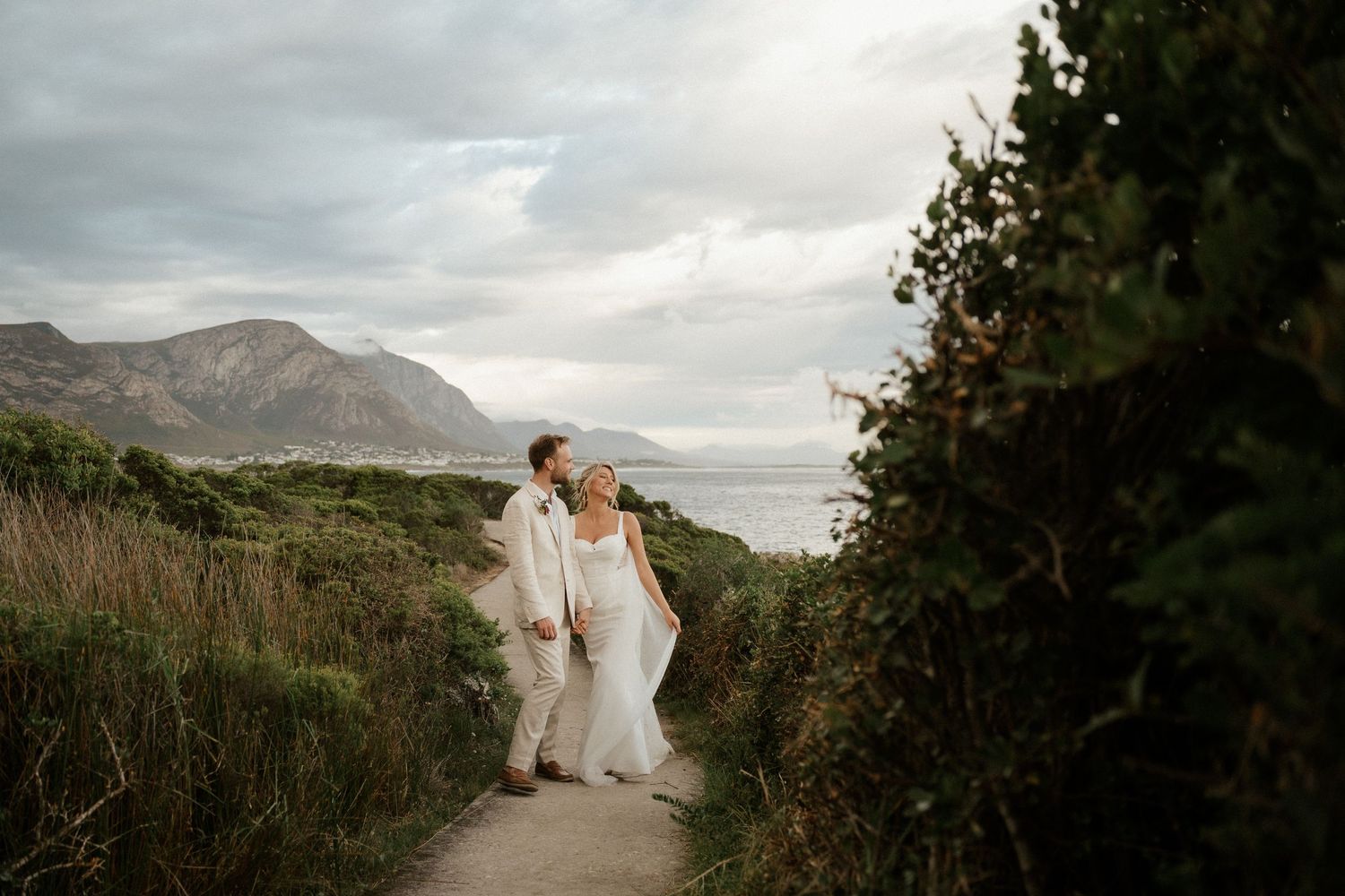 A couple pauses on a scenic coastal trail with mountains and ocean views.