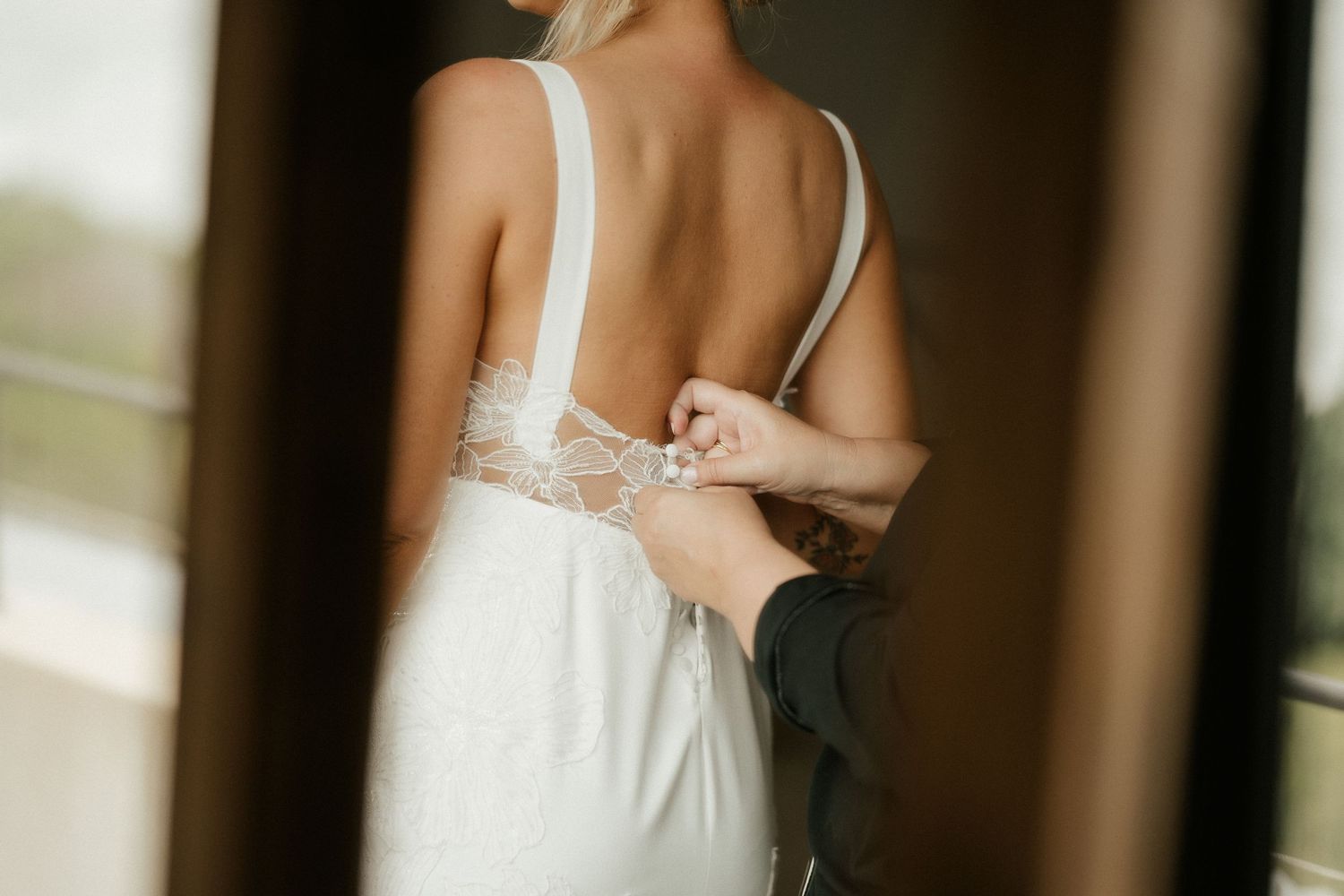 A close-up view of a bride's wedding dress being fastened from behind.
