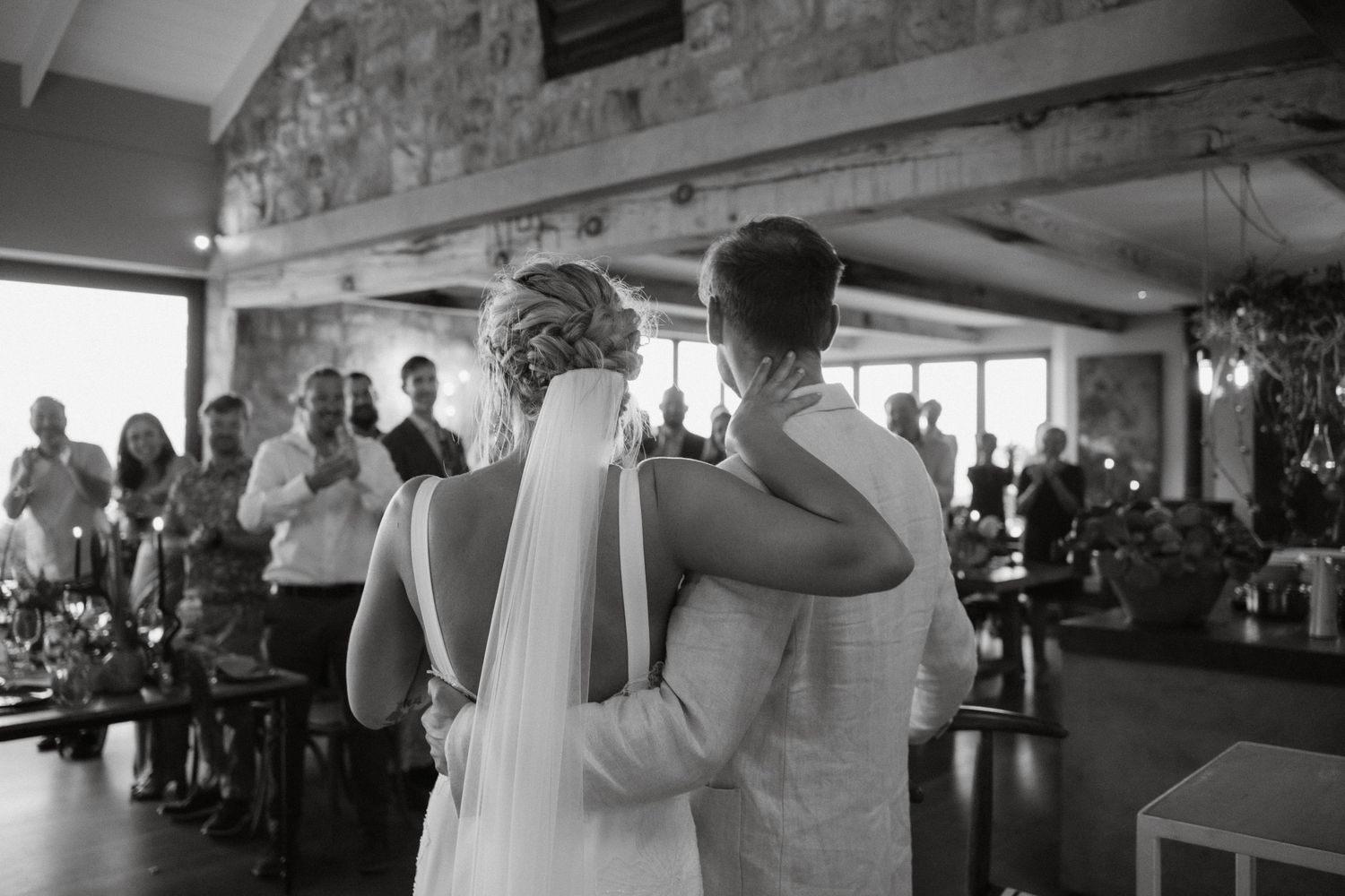 A black and white reception photo showing guests celebrating at a wedding venue.