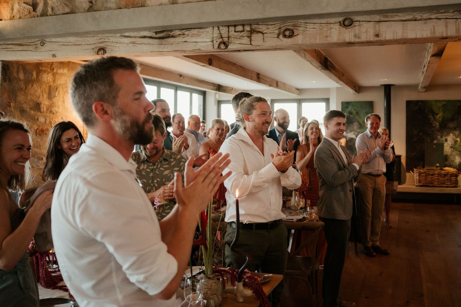 Guests applauding during a celebration in a rustic venue with exposed beams and ambient lighting.