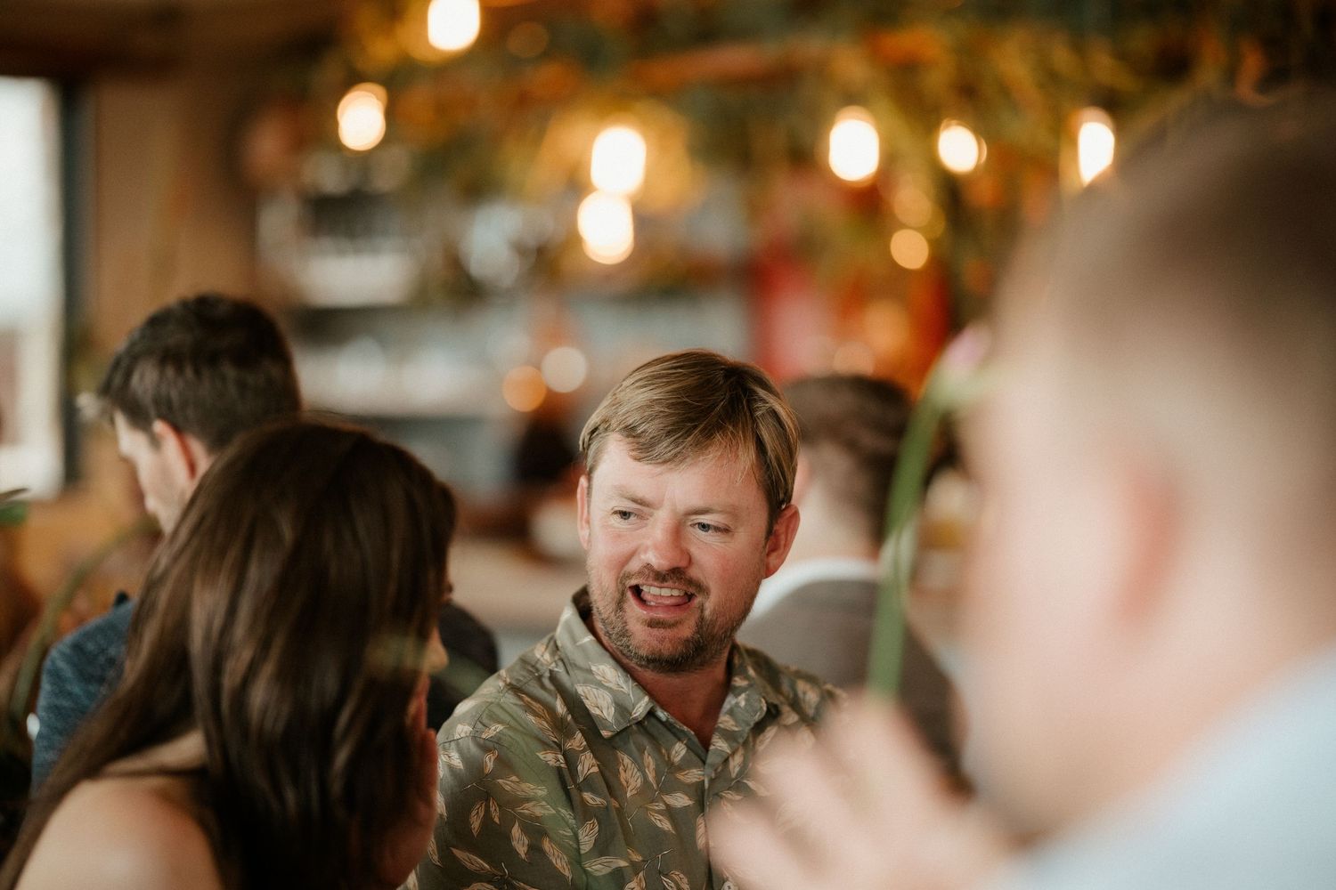 A casual social gathering with laughter and conversation in a warmly lit restaurant setting.