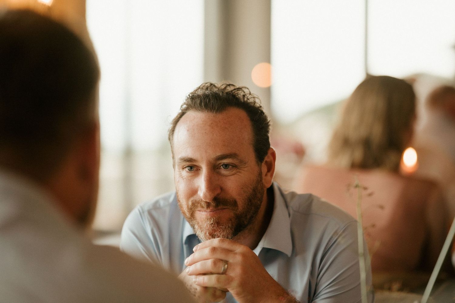 Man in casual attire listening intently during conversation at dining table.