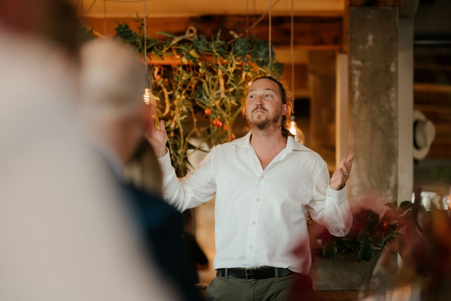 A person in a white shirt gestures expressively during what appears to be a wedding speech or toast.