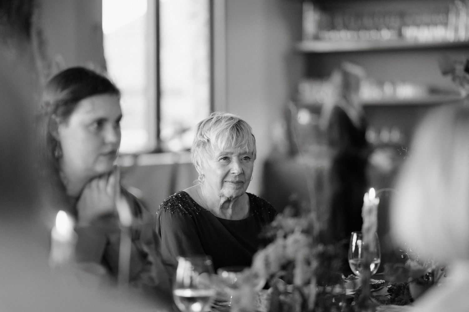 Black and white candid photo of guests dining by candlelight at an intimate gathering.