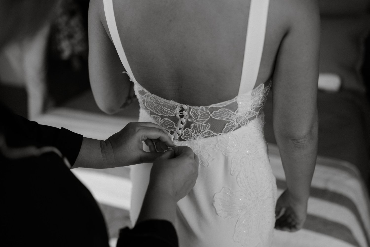 Black and white close-up shot of intricate lace detailing being fastened on the back of a wedding dress.