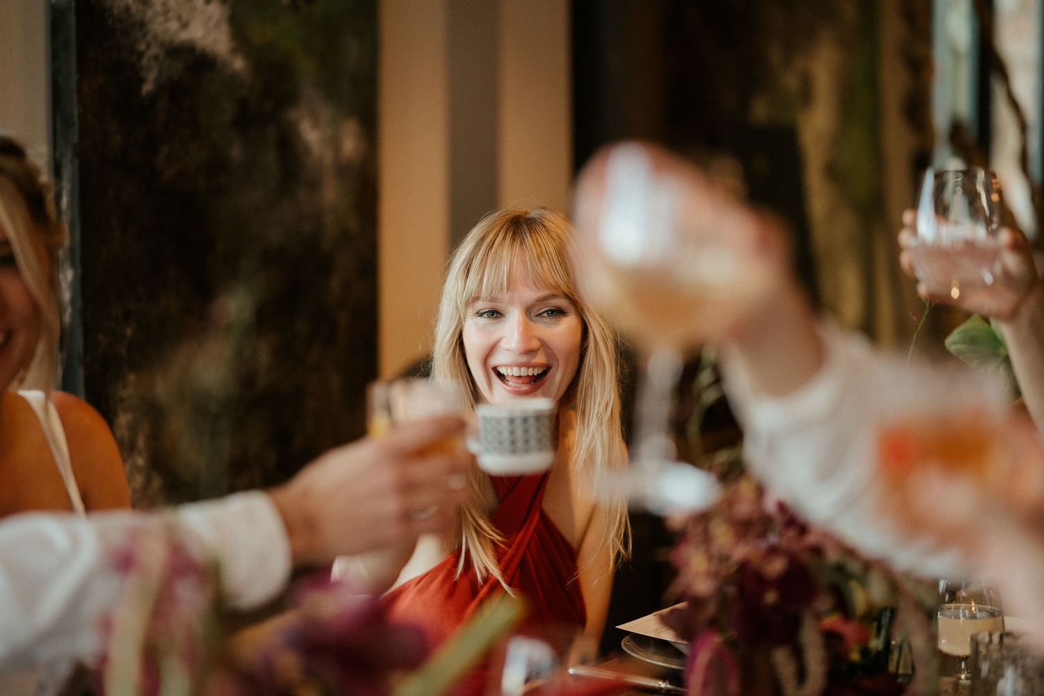 Wedding reception celebration with guests toasting and laughing at decorated venue.