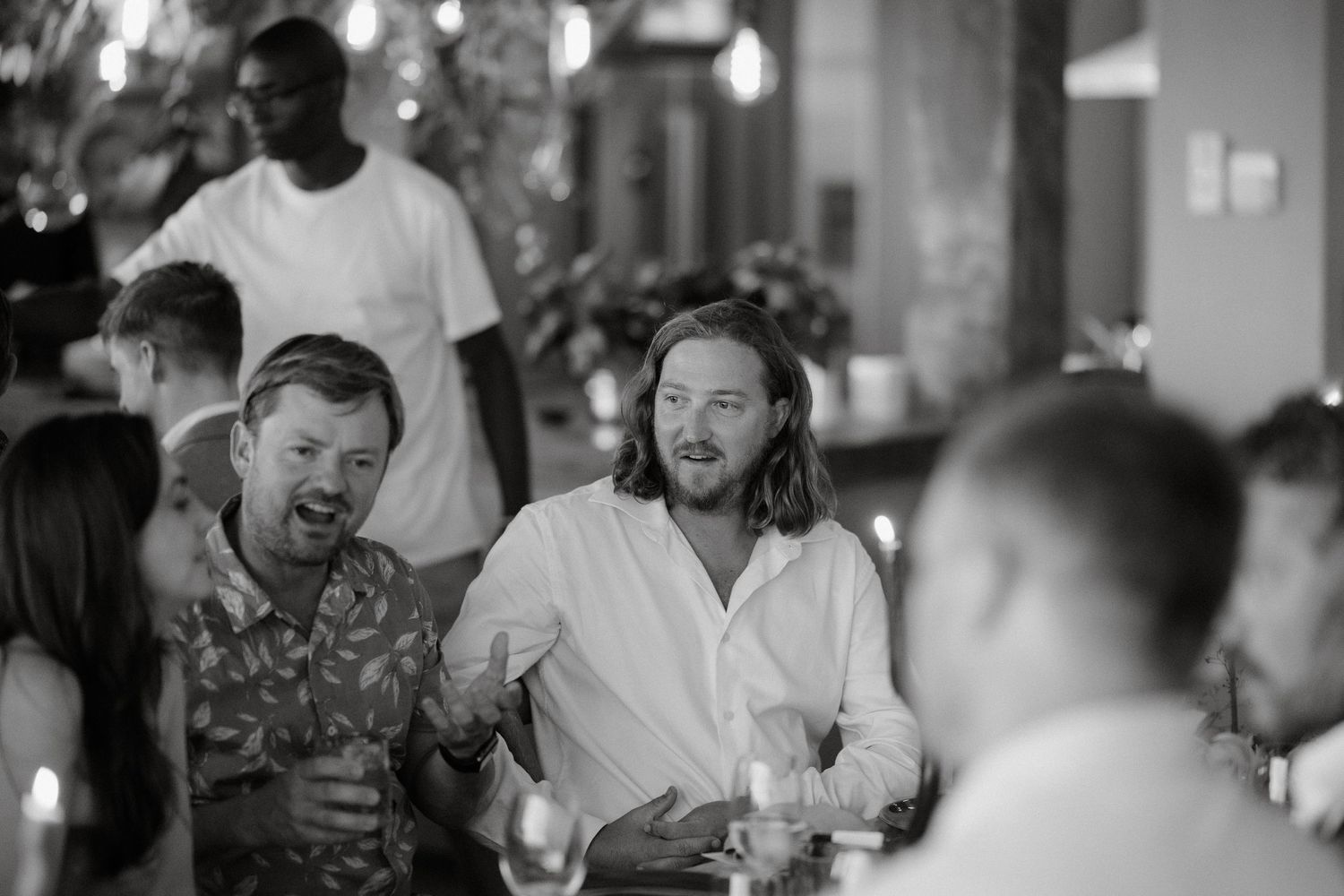 Black and white candid shot of guests laughing and socializing at a dinner party.