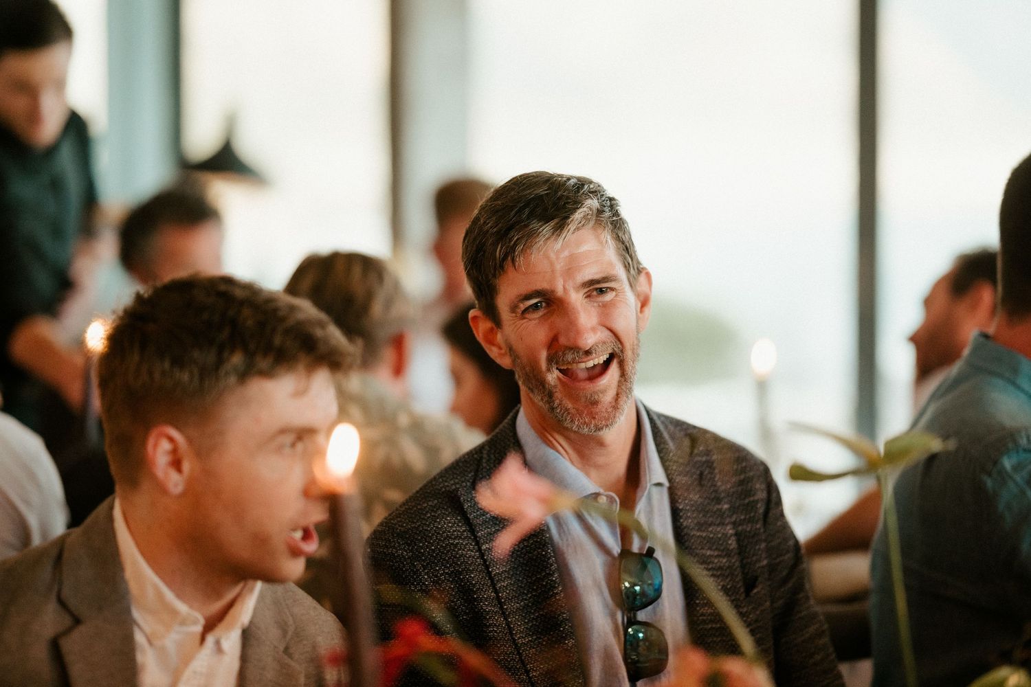Two guests share a candid laughing moment during a casual social gathering in a bright indoor setting.