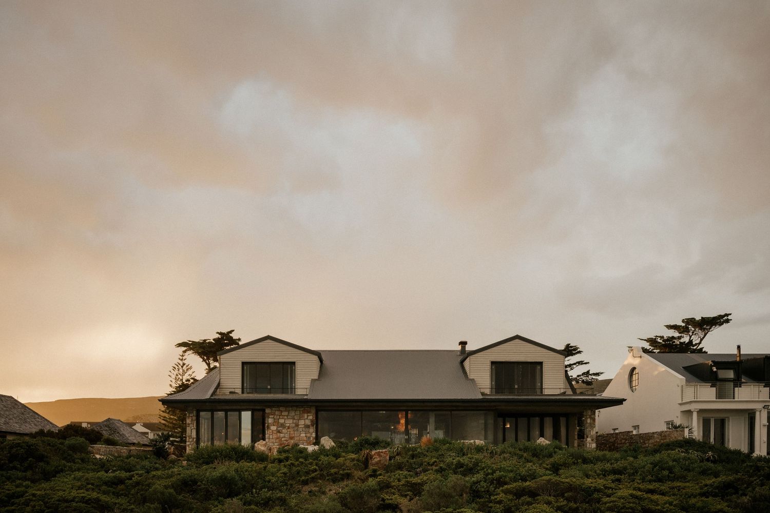 Modern white residential buildings set against a dramatic sunset sky with coastal vegetation.