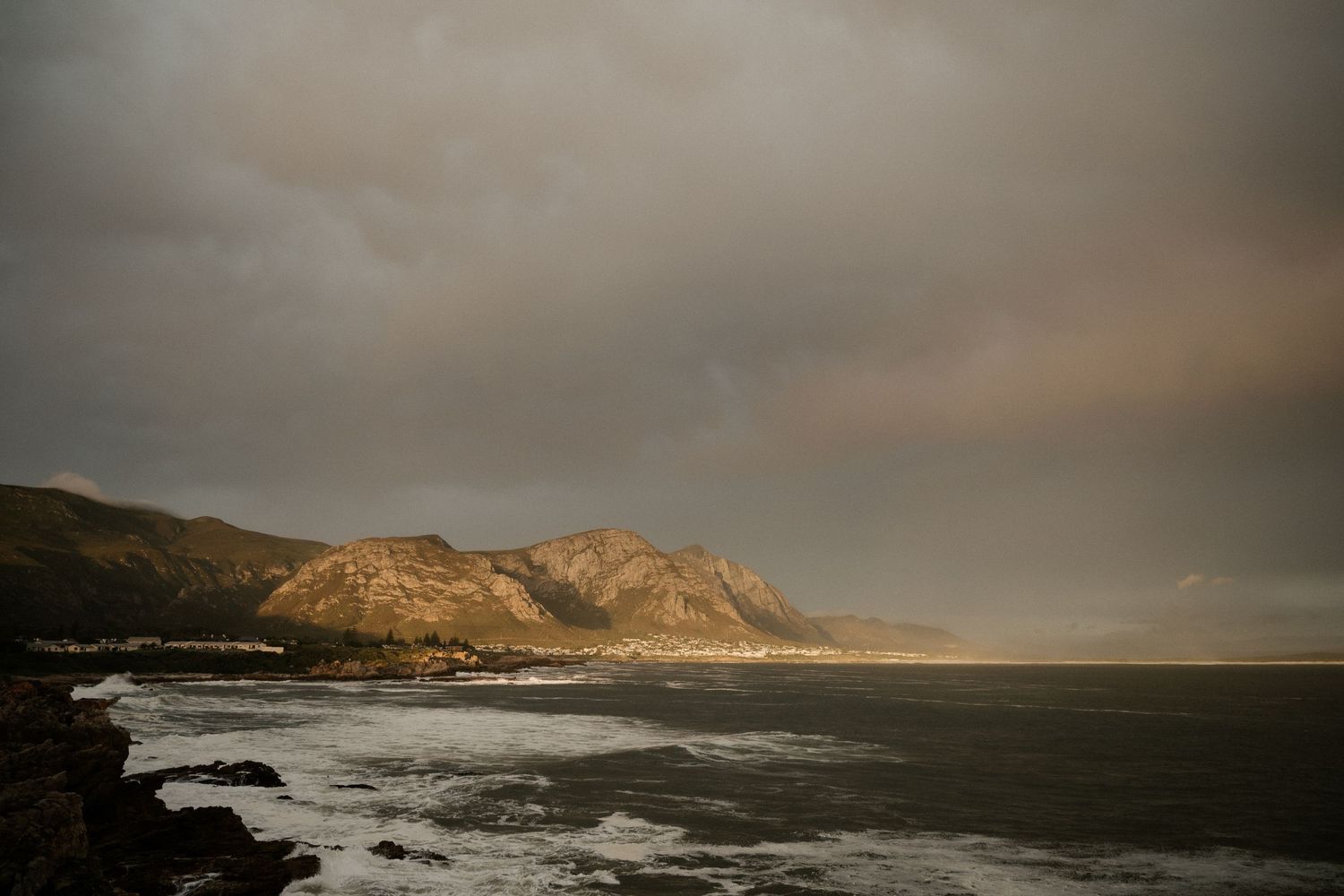 Dramatic coastline view with rugged cliffs and mountains against a moody sky.