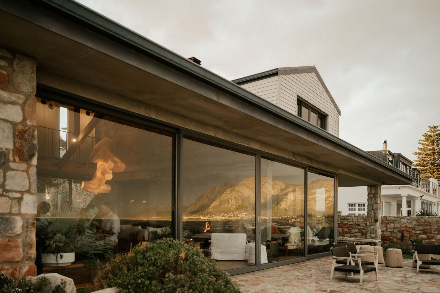 Modern building with large glass windows reflecting golden sunset light against stone exterior walls.