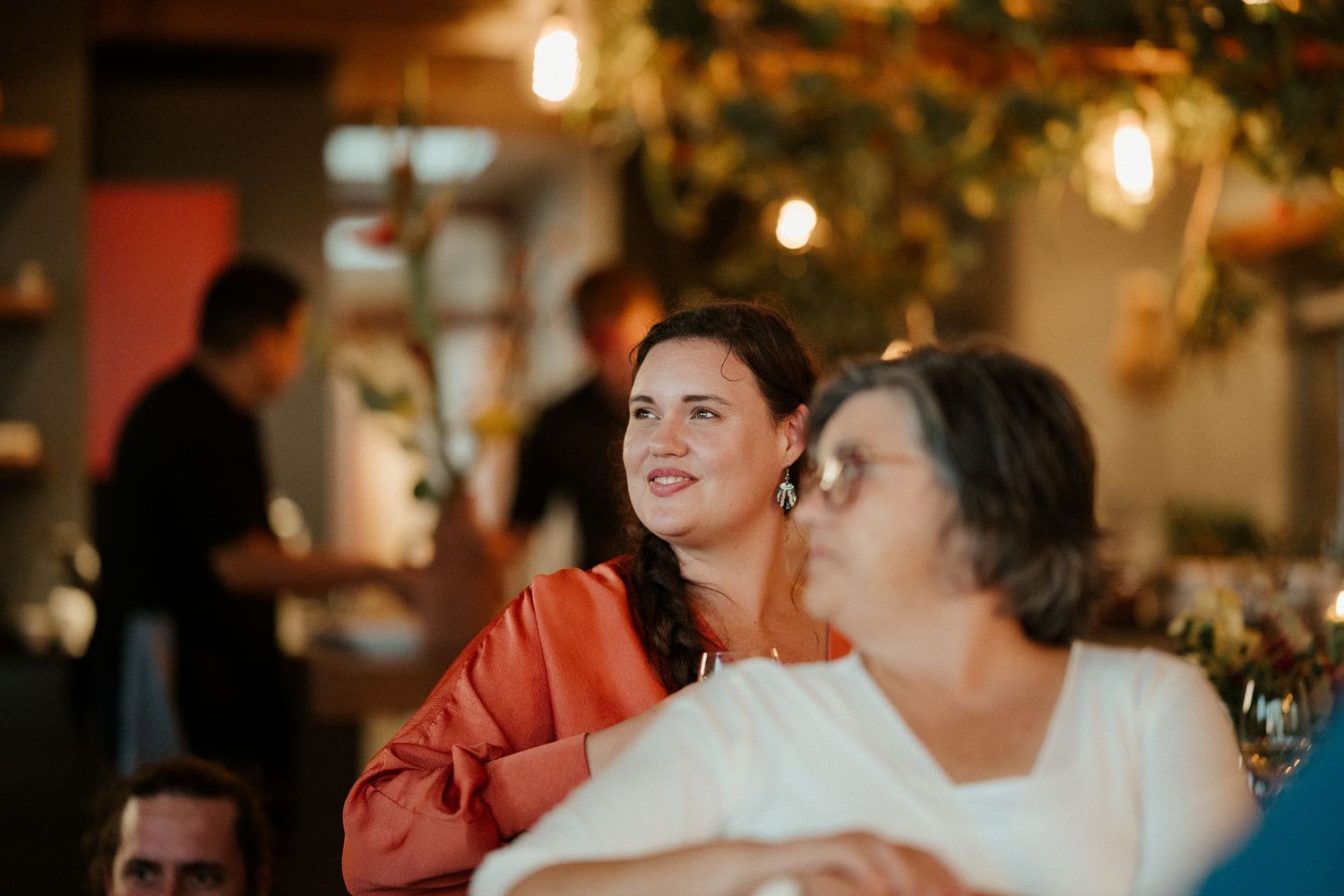Two diners enjoying an evening at a warmly lit restaurant with hanging pendant lights and festive decor.