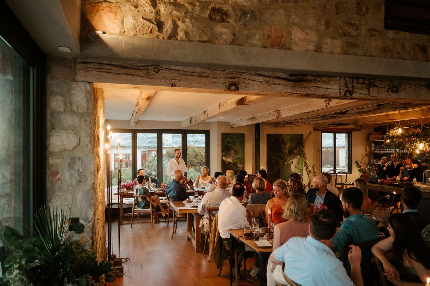 Rustic restaurant interior filled with diners under exposed beam ceilings and stone walls.