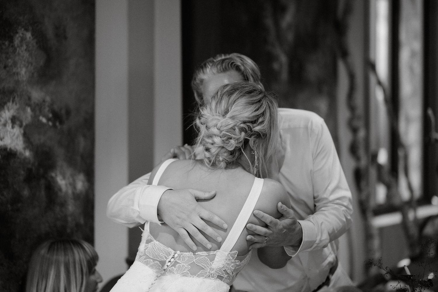 A black and white candid moment shows two people embracing during a wedding celebration.
