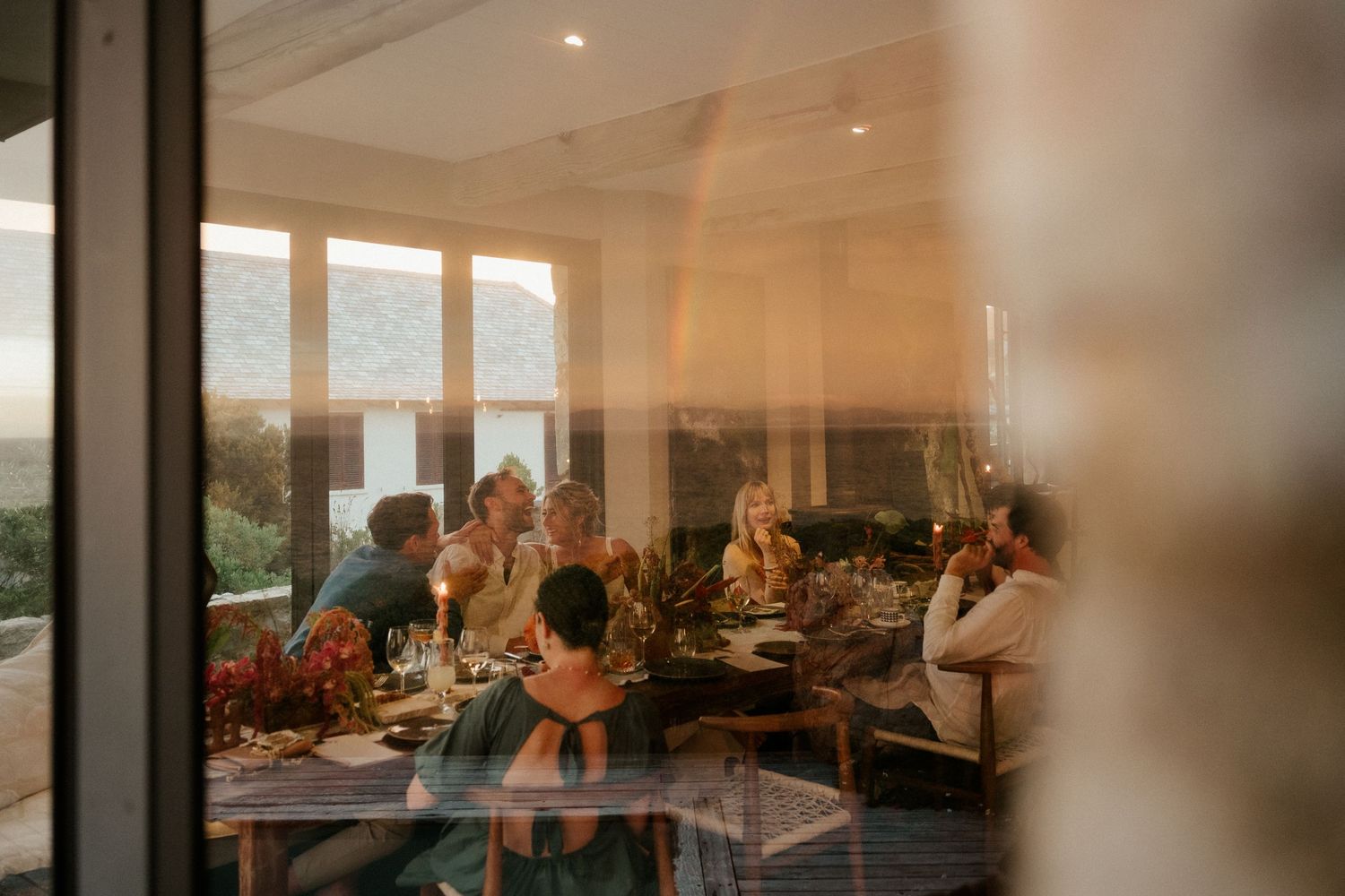 Warm sunset light streams through windows at dinner gathering with guests seated around table.
