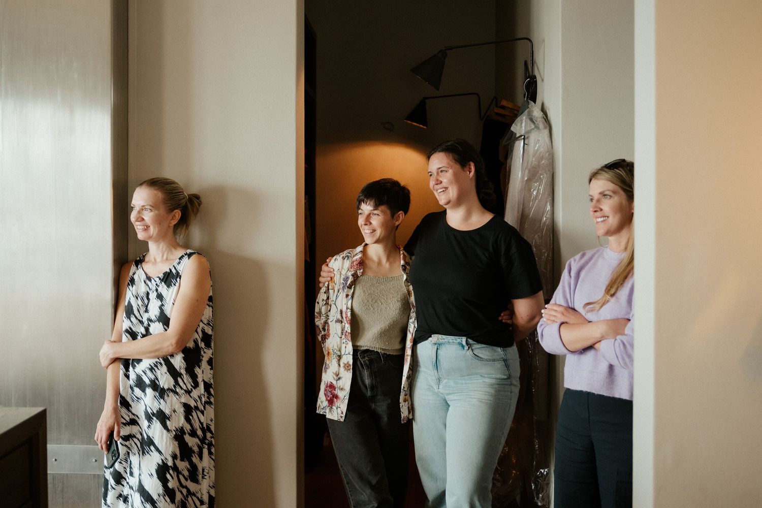A group of friends standing together in casual attire against a light colored wall in an interior space.