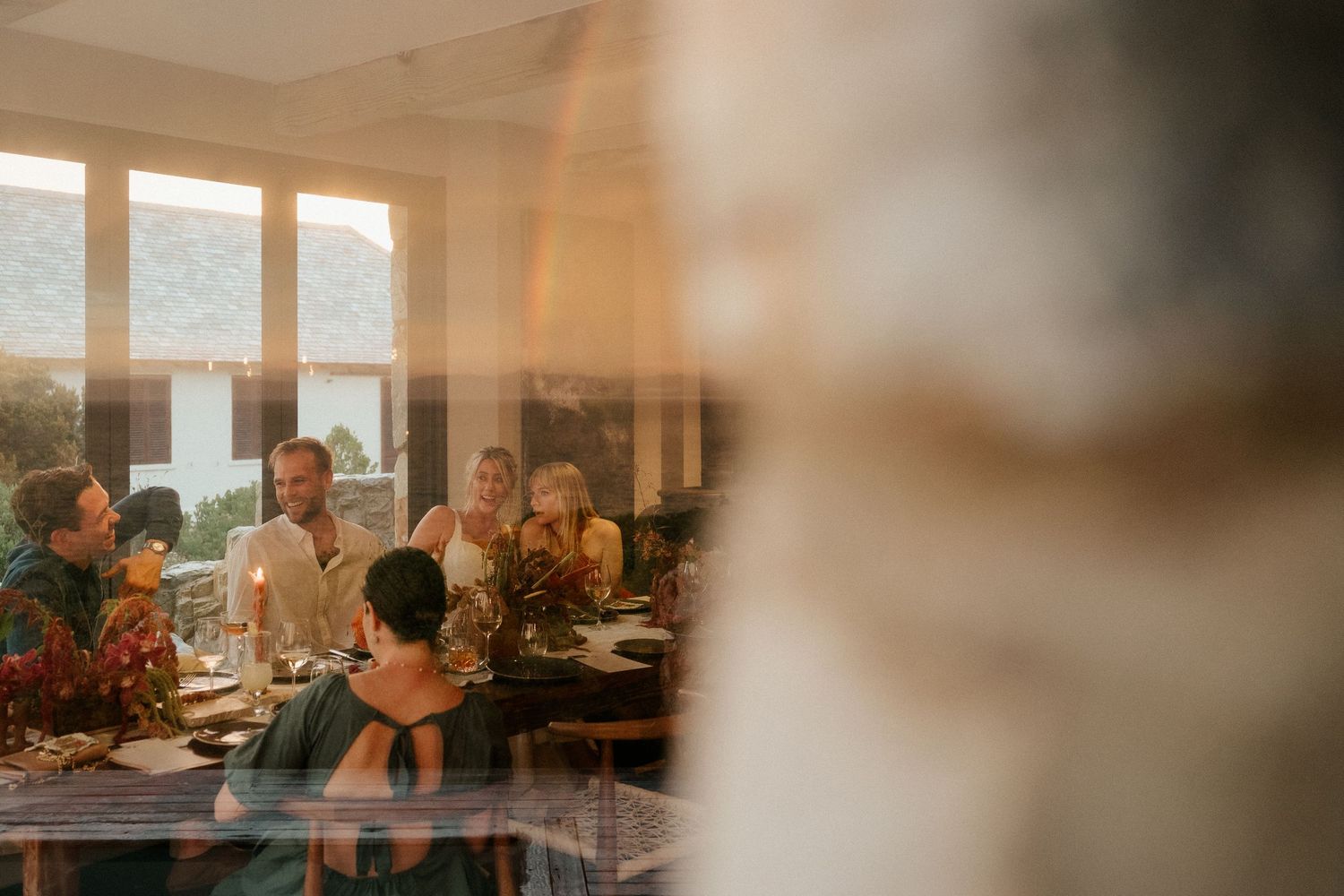 Sunlight streams through windows during an intimate wedding reception dinner with guests seated at tables.