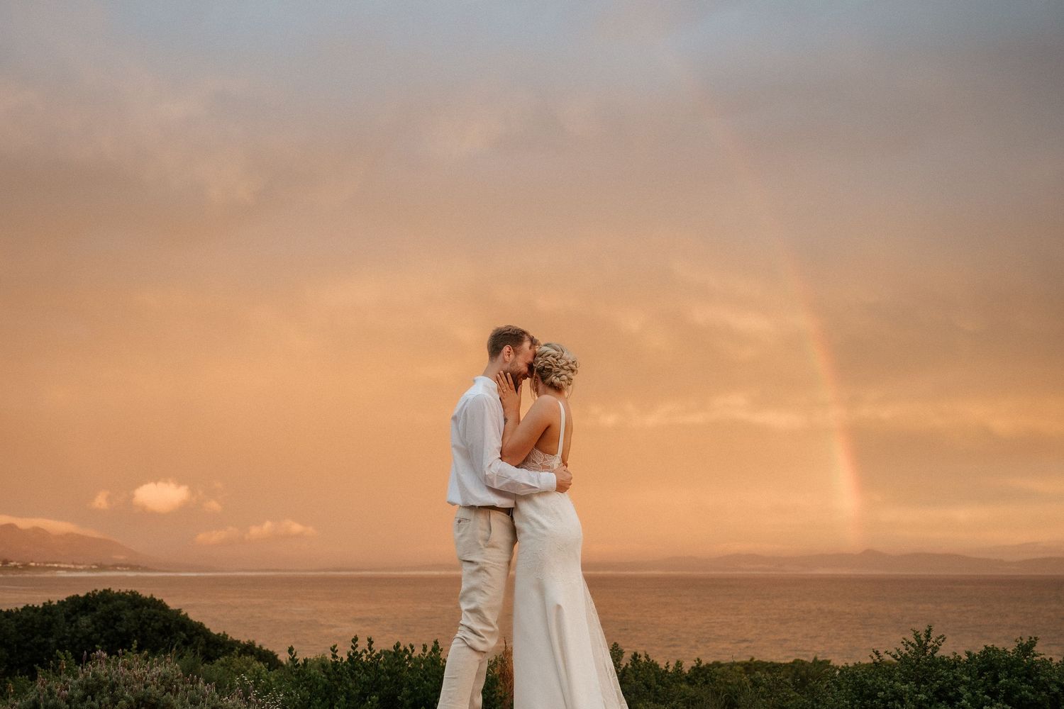 A romantic sunset moment with a rainbow appearing over the ocean horizon.