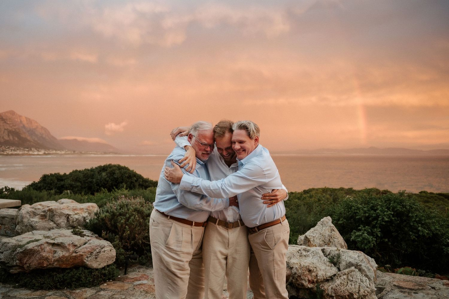 A group shares a warm embrace during sunset overlooking a coastal landscape.