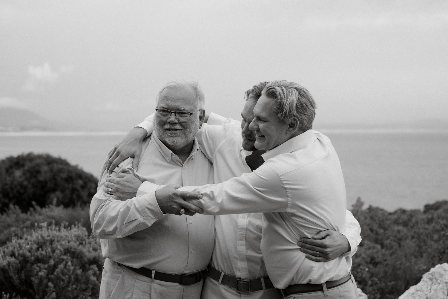 Black and white photograph of three people sharing a heartfelt moment outdoors.
