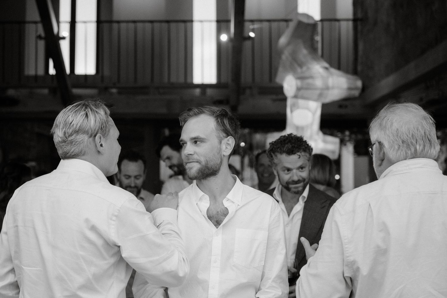 A black and white candid photo captures intimate moments between wedding guests.