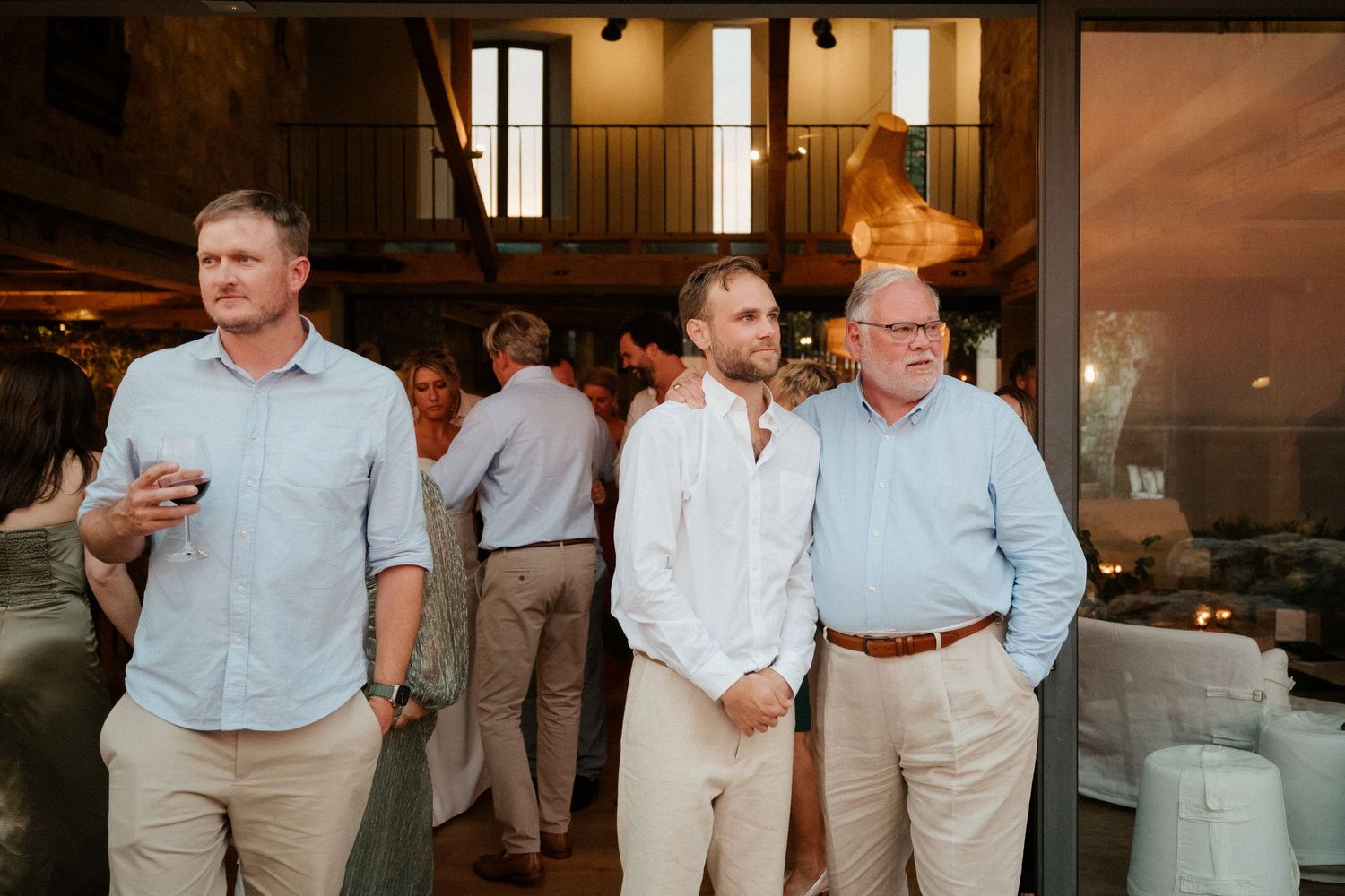 Three guests in casual attire converse together during an indoor reception event.